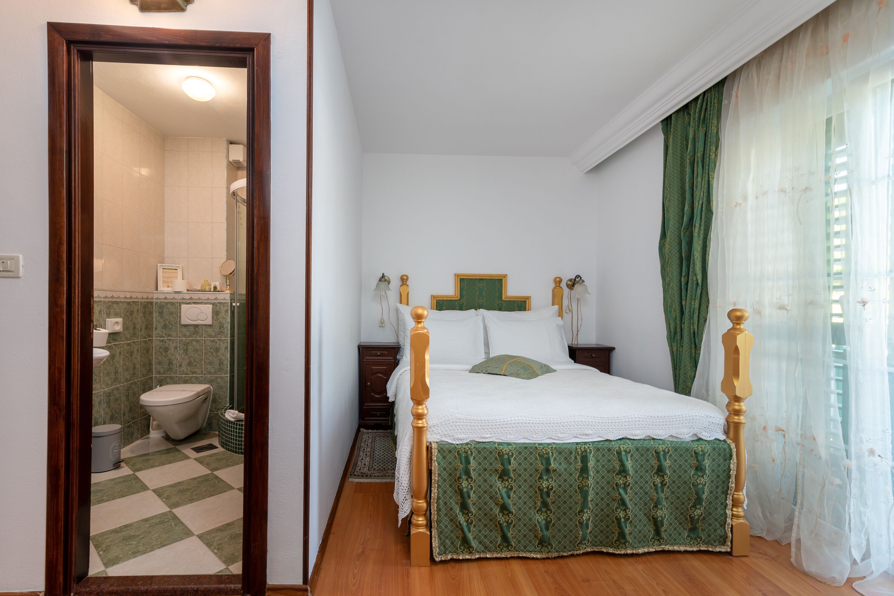 Un dormitorio con una cama de madera, un edredón verde y un baño visible a través de una puerta abierta.
