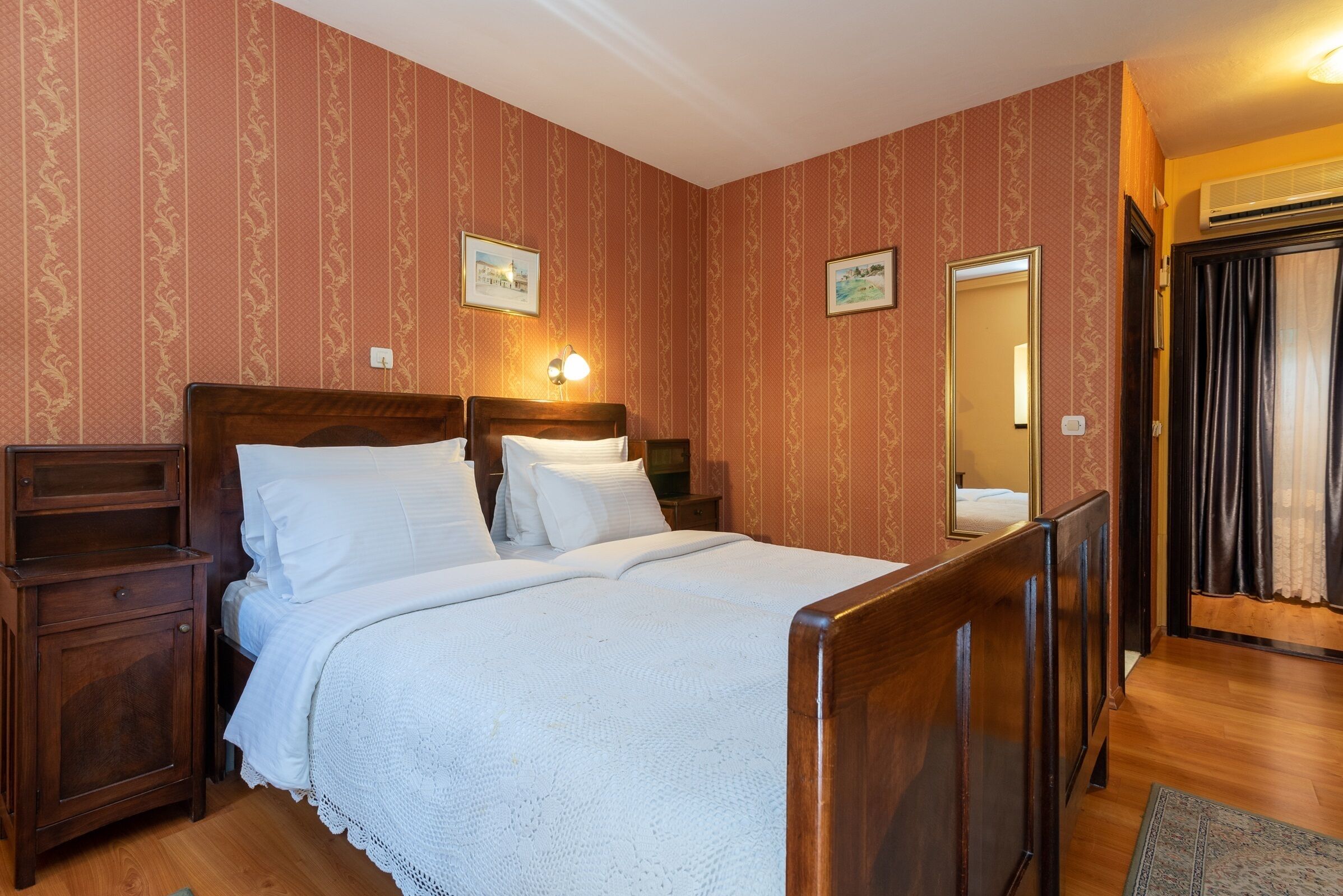 A neatly arranged bedroom with a wooden bed, a nightstand, a bedside table, and a mirror.