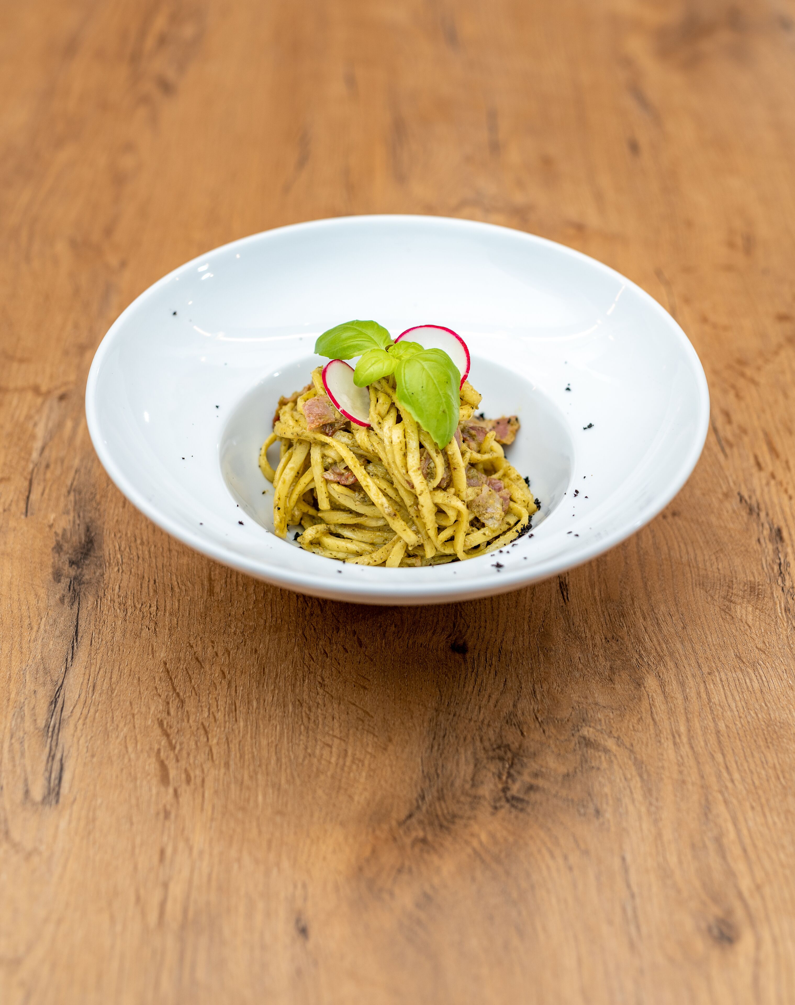 A white plate with pasta, basil, and radish on a wooden table.
