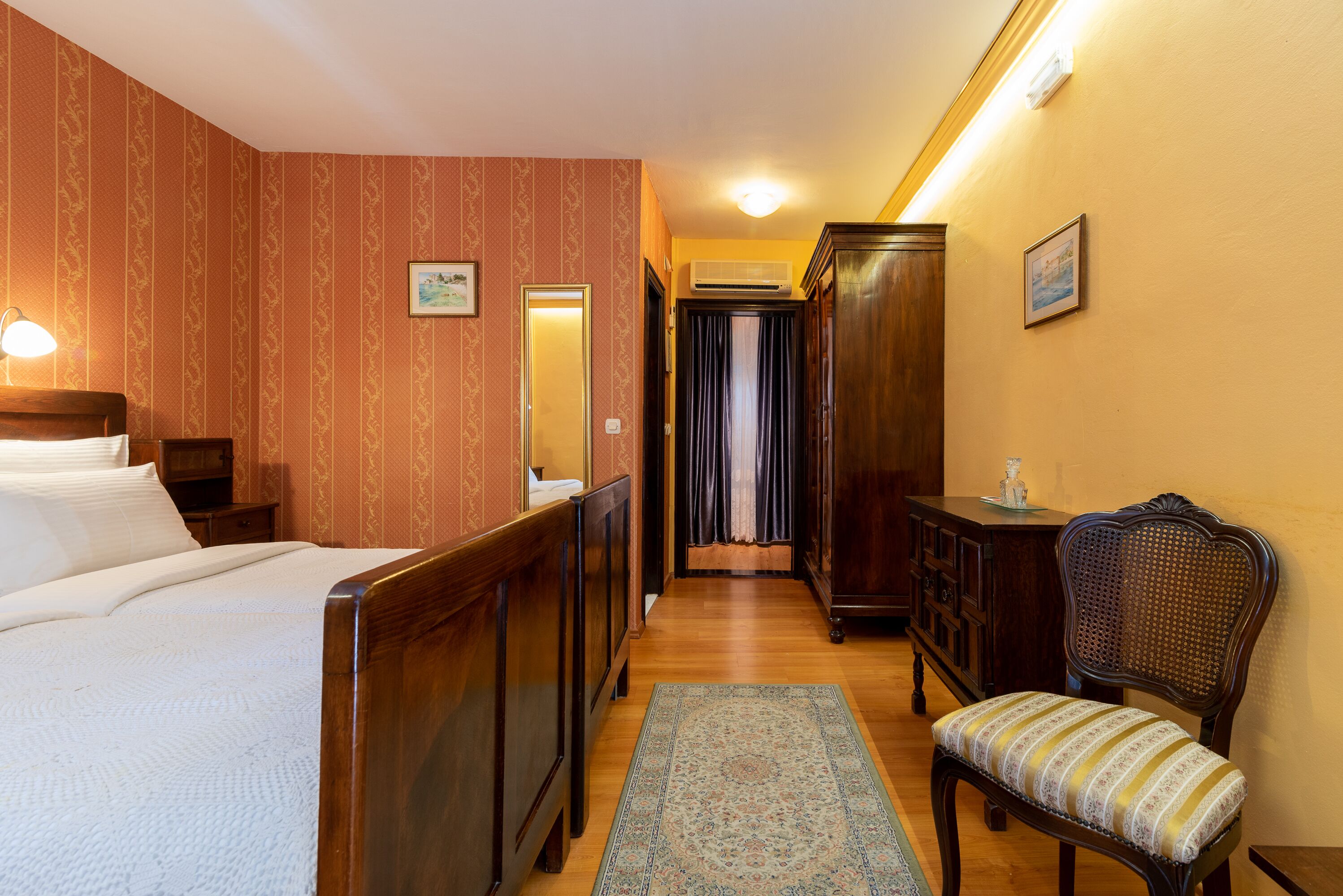 Hotelkamer met een bed, houten meubels, een stoel en een gang met een deur en gordijnen.