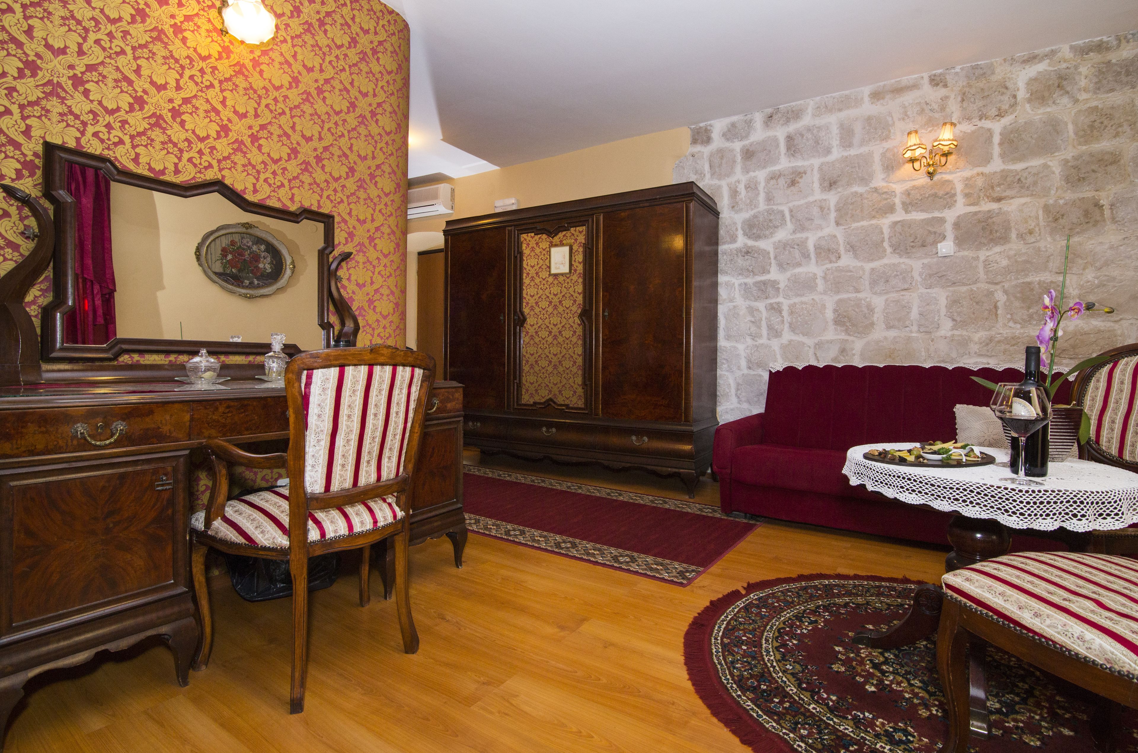 A room with a wooden dresser, a chair, a red sofa, a stone wall, and a small round table with a vase and a bottle.