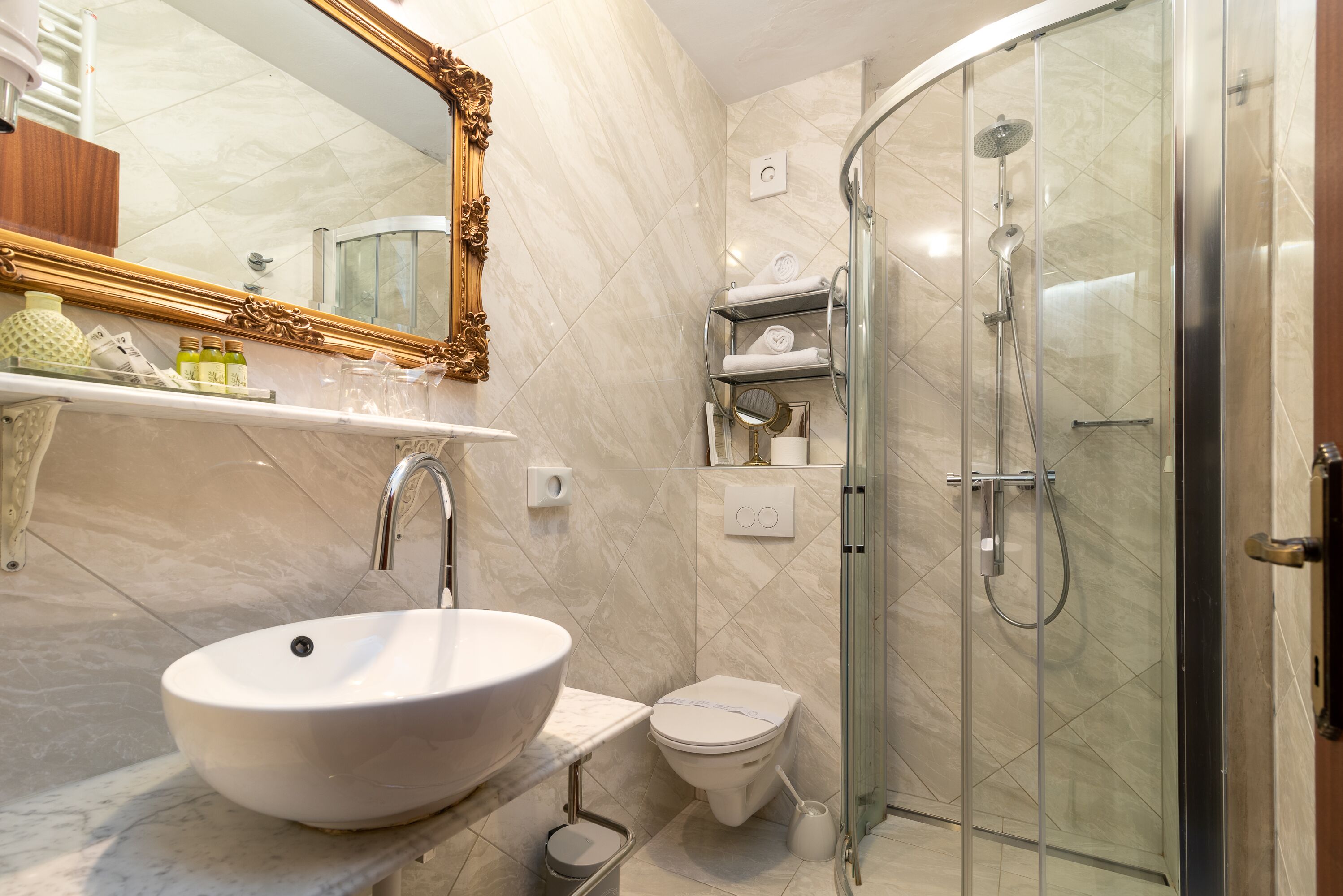 Une salle de bain moderne dotée d’un grand lavabo ovale, de toilettes, d’une douche à parois de verre et d’un meuble-lavabo avec des étagères.