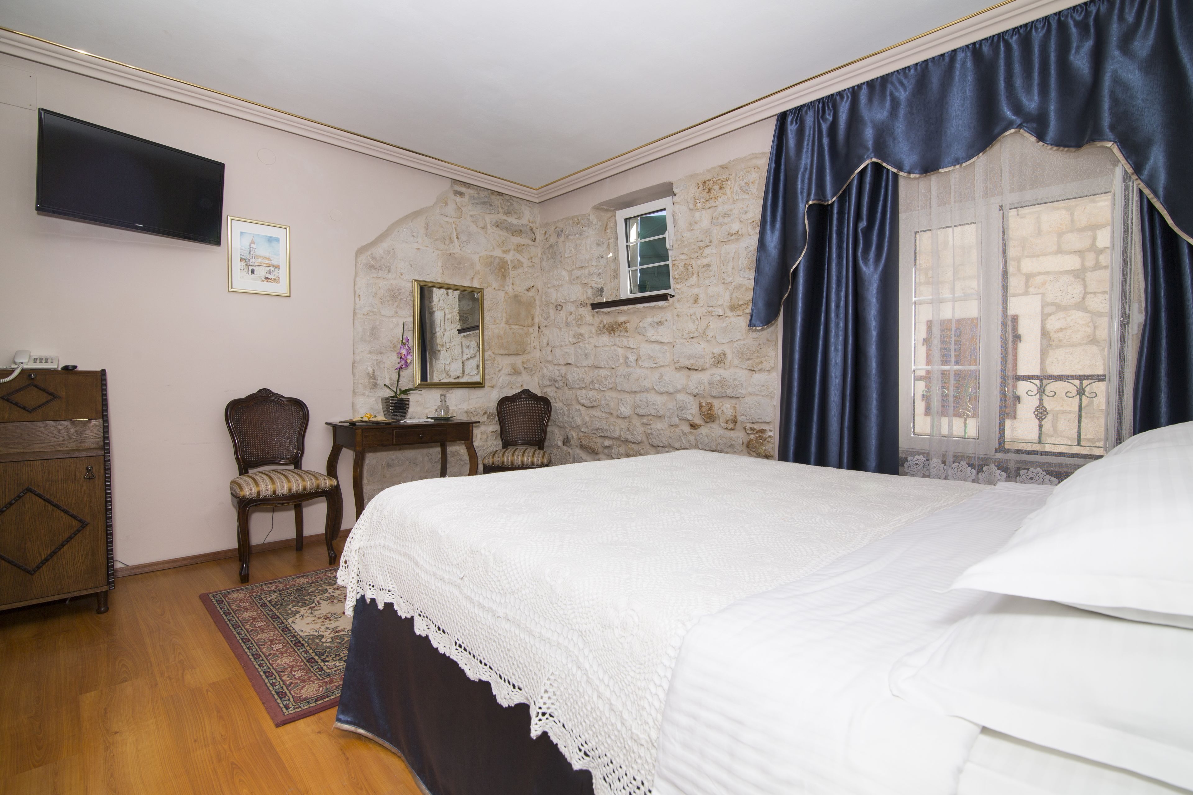 A bedroom with a bed, a dresser, a television, a chair, a small table, and a window with curtains.