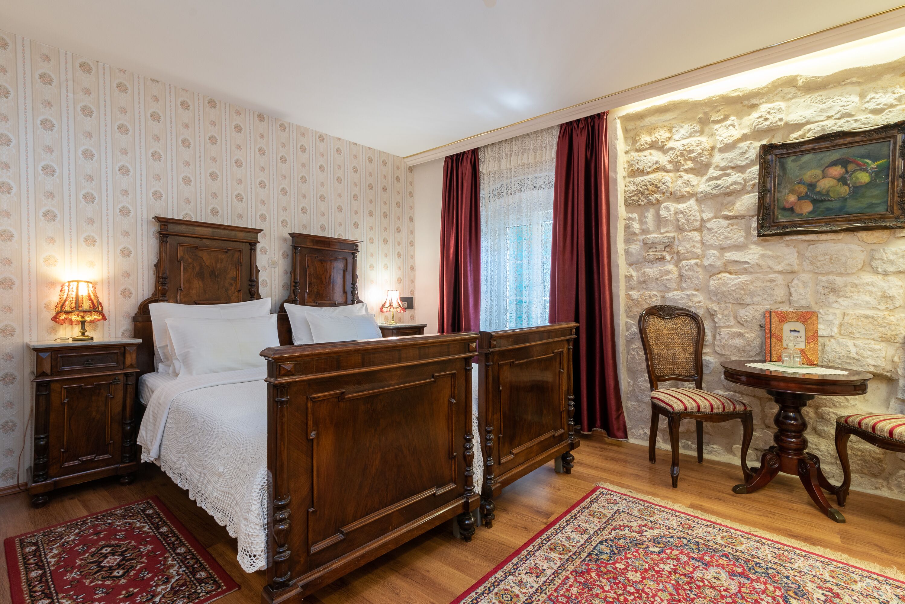 Un dormitorio tradicional con una cama con dosel de madera, una mesita de noche con lámpara, una silla y una pequeña mesa.