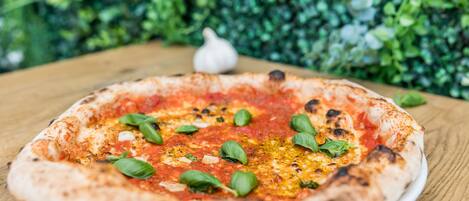 A pizza on a white plate with a wooden table and a green leafy background.