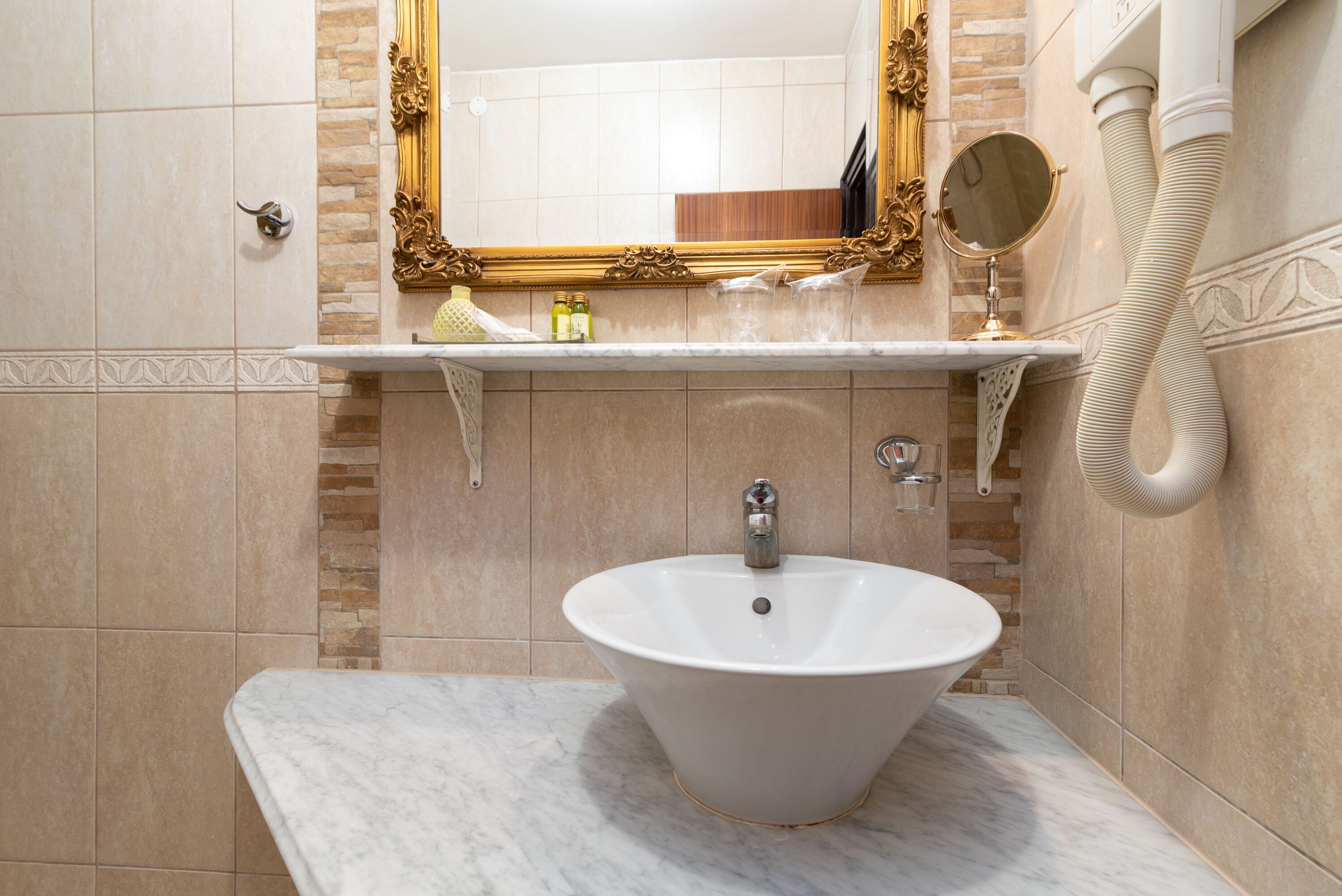 A bathroom with a white pedestal sink, a gold-framed mirror, and a marble countertop.
