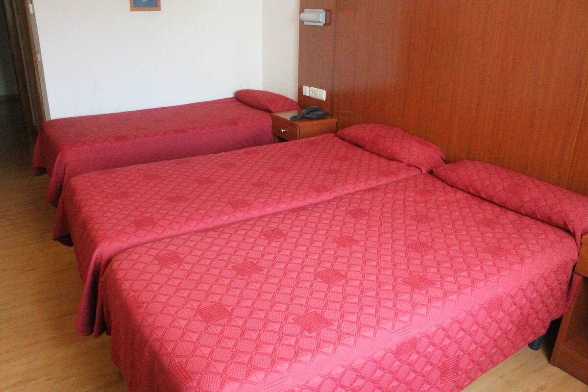 A hotel room with two single beds, a wooden wardrobe, and a bedside table with a telephone.