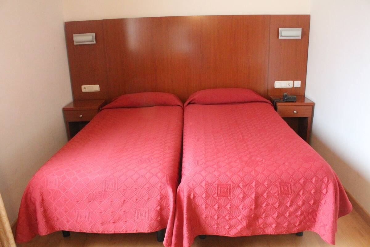 A double bed with a wooden headboard, two bedside tables, and a red bedspread.
