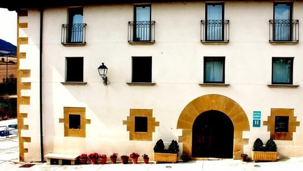 A hotel facade with a symmetrical design, featuring a central arched entrance, multiple windows with balconies, and a sign indicating the hotel name. - Agorreta (Galar)