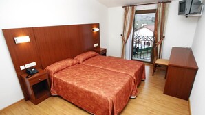 A hotel room with a wooden headboard, a bed with a red bedspread, a bedside table with a phone, a desk with a chair, and a TV mounted on the wall. - Agorreta (Galar)