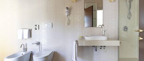 Un baño moderno con bidé, inodoro, lavabo y ducha con mampara de vidrio.
