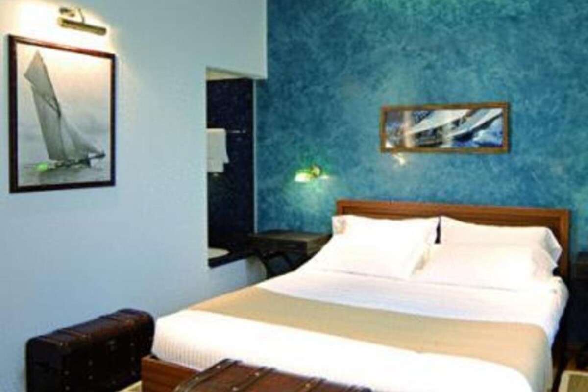 A hotel room with a bed, a wooden headboard, a nightstand, a lamp, and a framed picture on the wall.