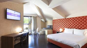 Habitación de hotel con una cama grande, un escritorio y un televisor que muestra la frase 'STAY TUNED'.