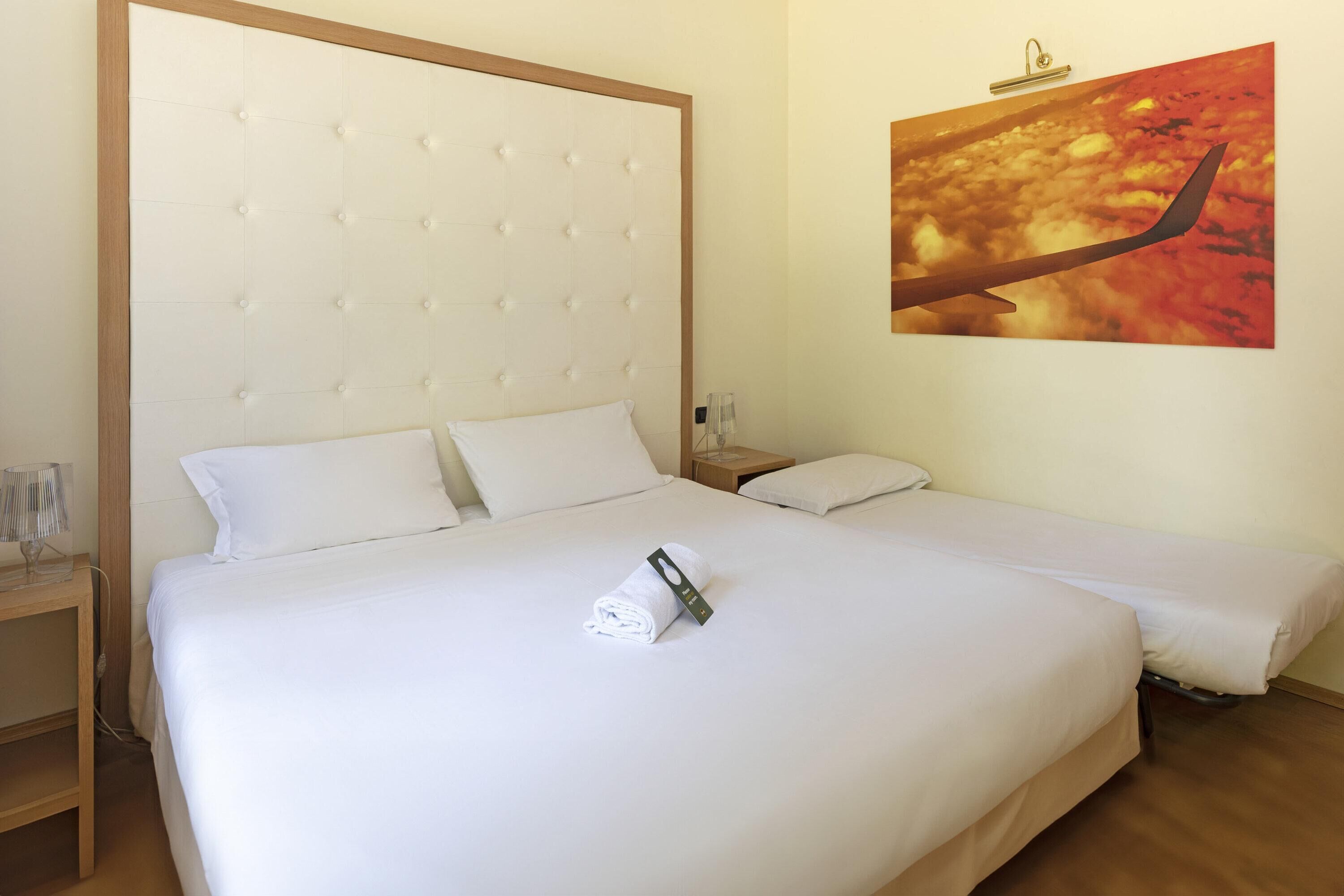 Een hotelkamer met een groot bed, een kleiner bed en een nachtkastje met een lamp.