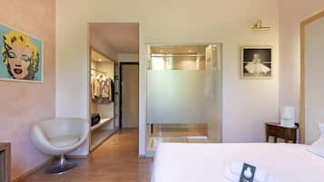 Habitación de hotel con cama, una silla, armario y baño visible a través de una puerta de vidrio.