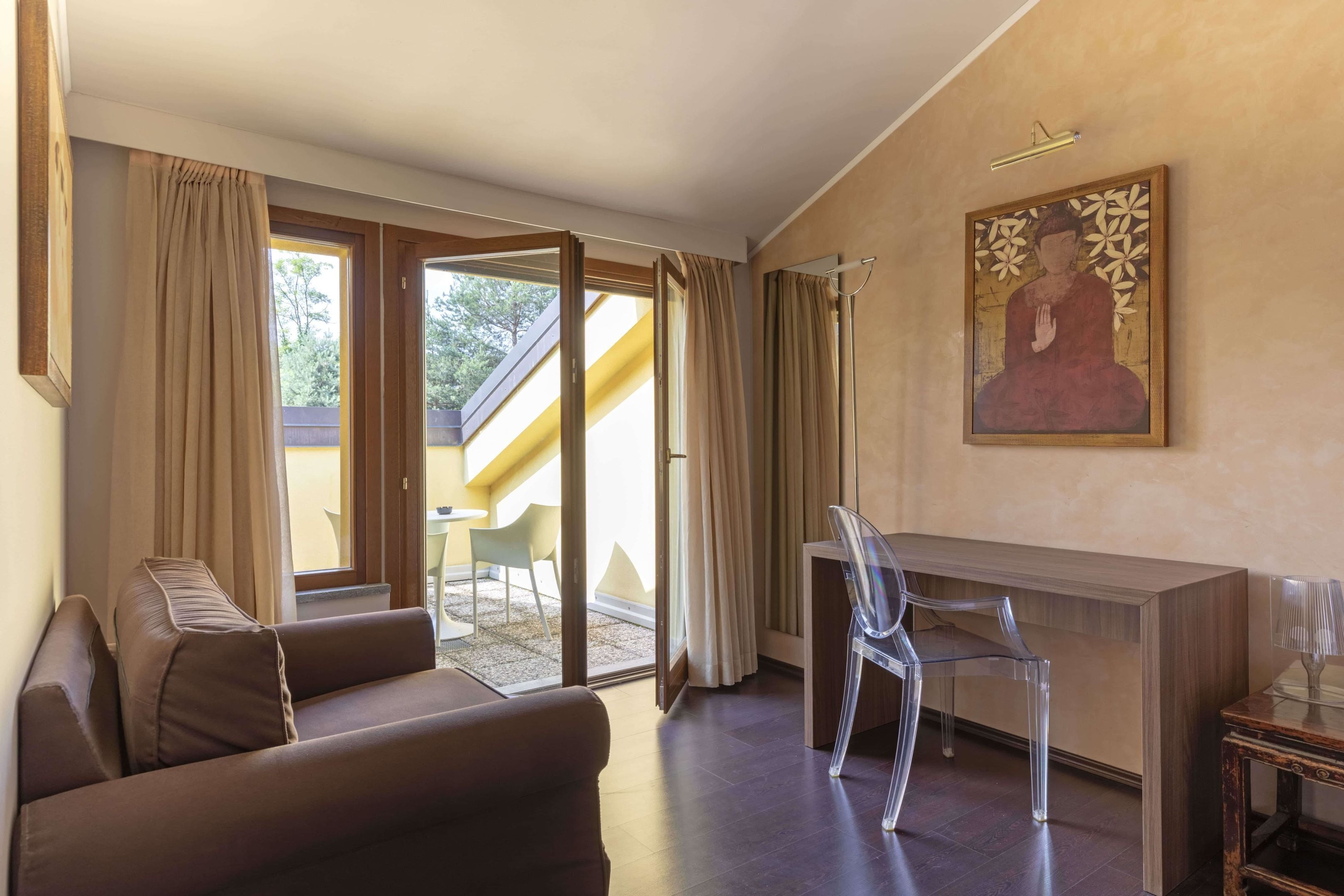 Una habitación moderna con un sofá, un escritorio y una silla. Hay una puerta corrediza de vidrio que da a un espacio exterior.