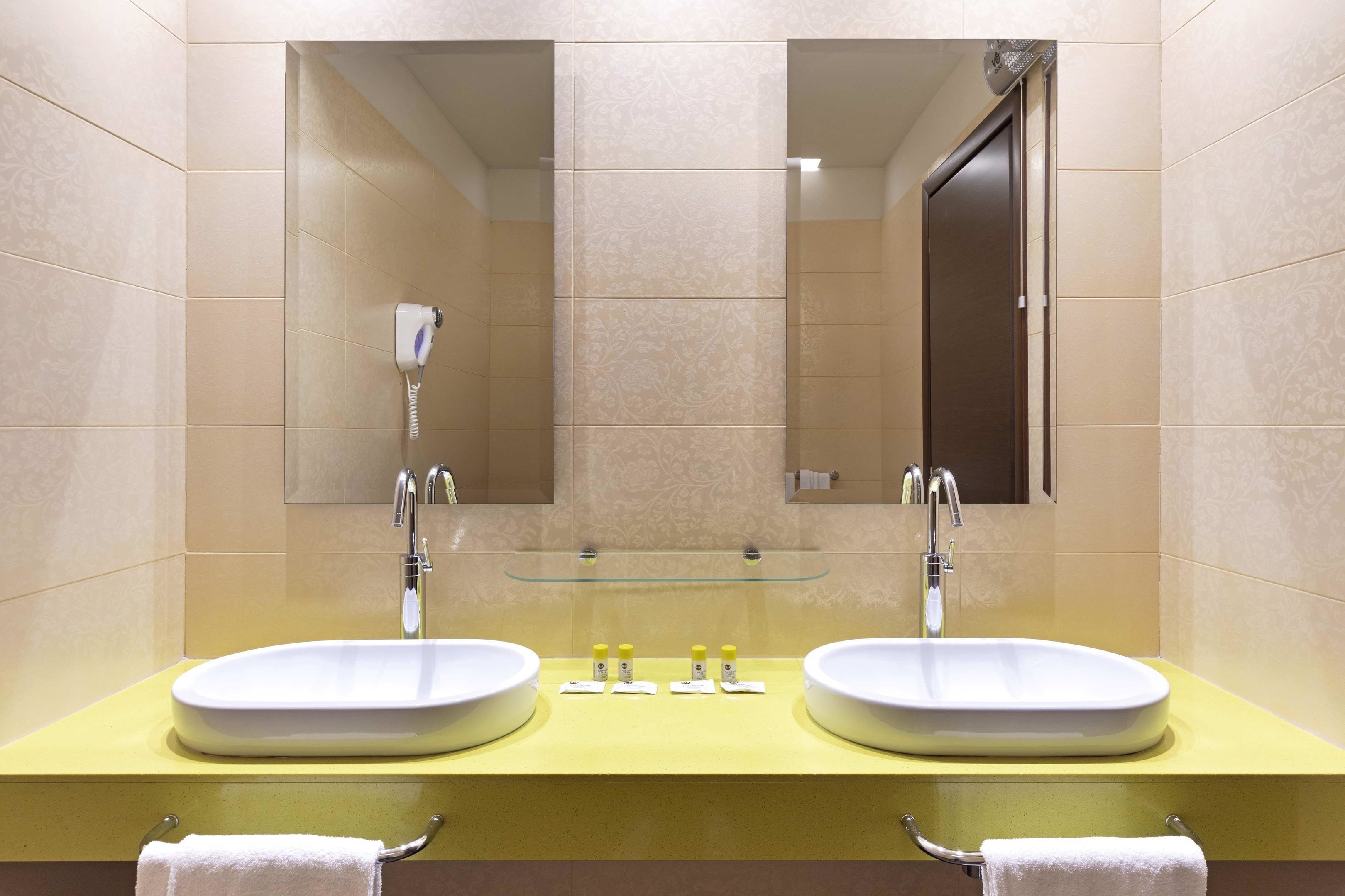 Un baño con dos lavamanos, un estante de vidrio y un espejo.