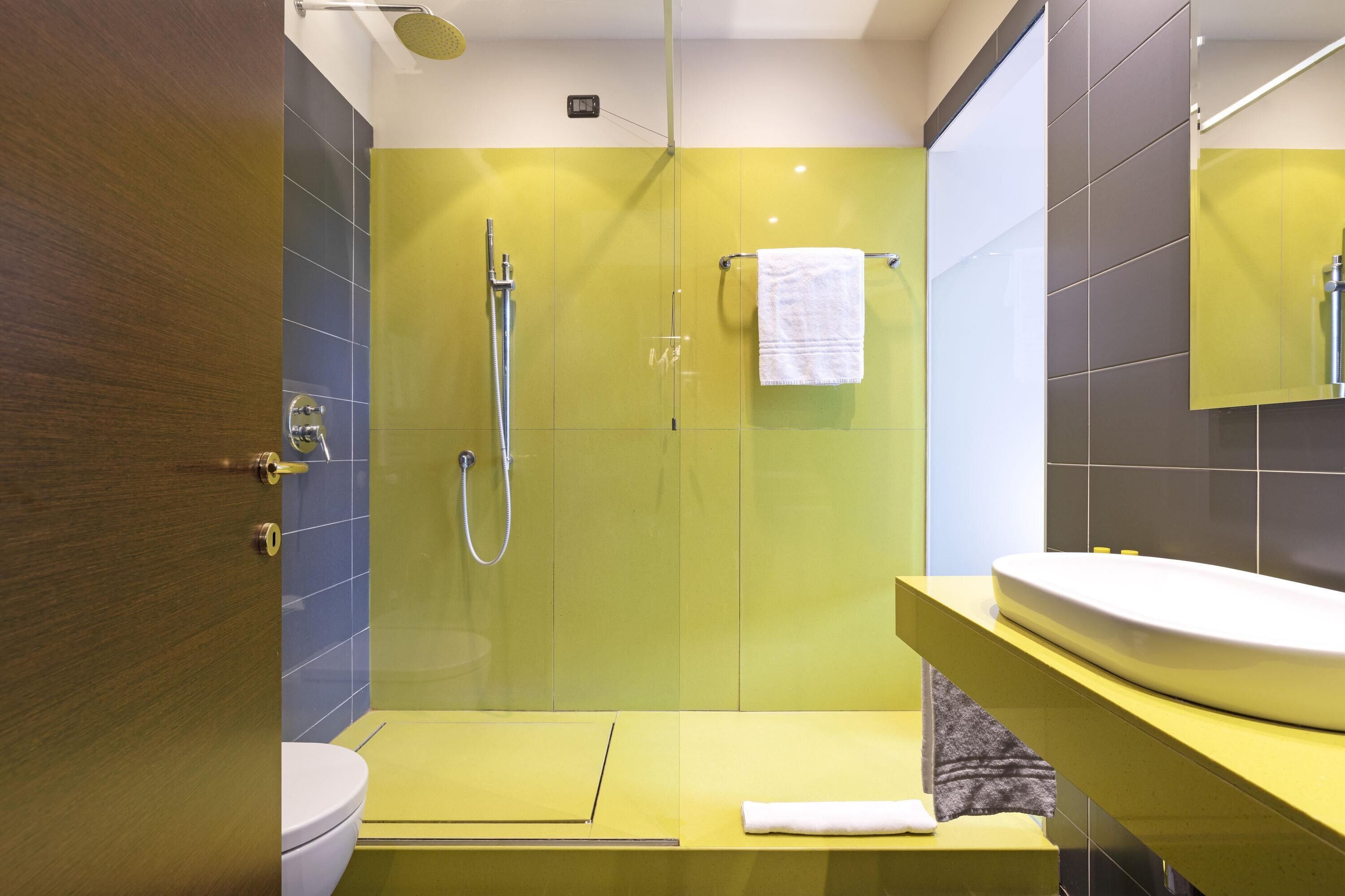 Un baño moderno con ducha acristalada, lavamanos blanco y tocador amarillo.