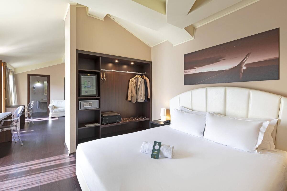 A hotel room with a large bed, a wardrobe, a desk, and a chair.