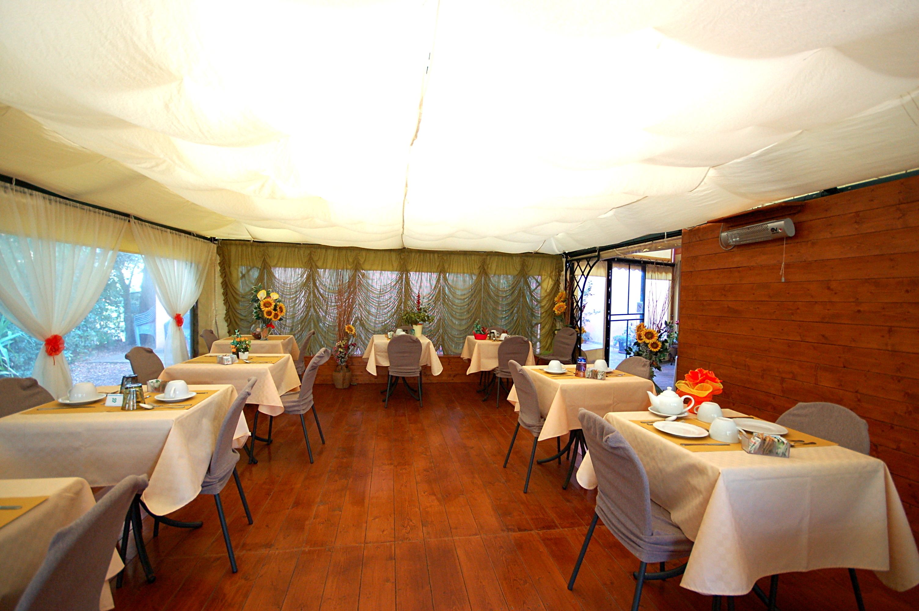 A tented dining area with tables set for service, featuring a wooden floor and white tablecloths.