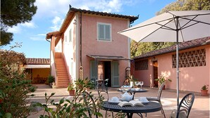 Un espace patio aménagé avec du mobilier d’extérieur, une table dressée pour les repas et un grand parasol offrant de l’ombre.