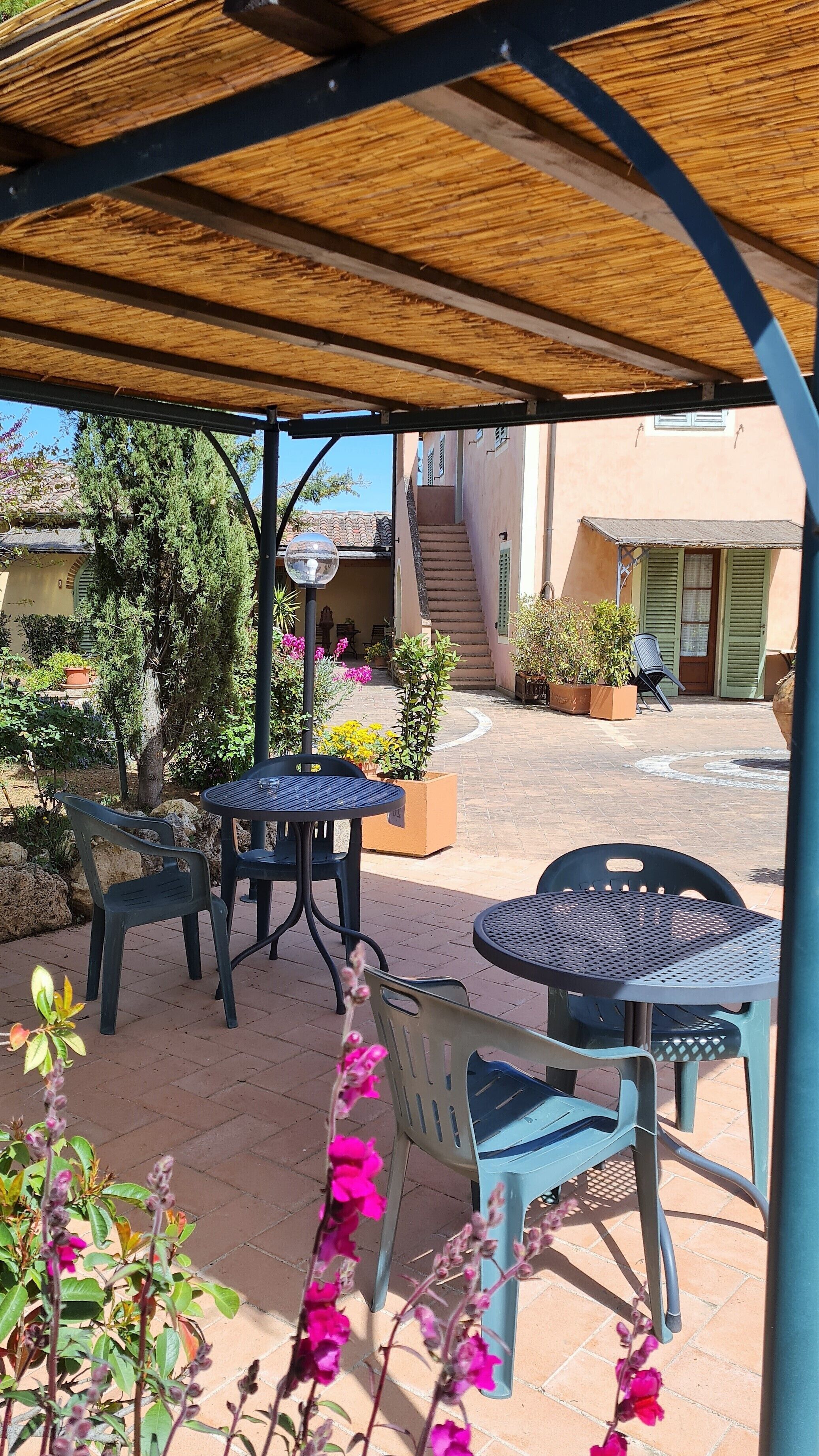 An outdoor patio area with metal tables and chairs, surrounded by potted plants and flowers.