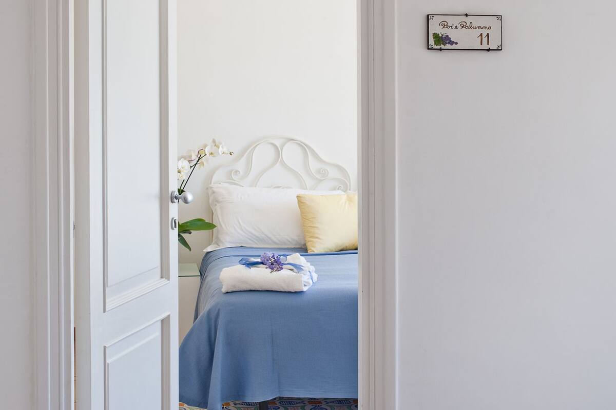 Ein Schlafzimmer mit einem weißen Bett, blauer Bettwäsche und einer kleinen Topforchidee.