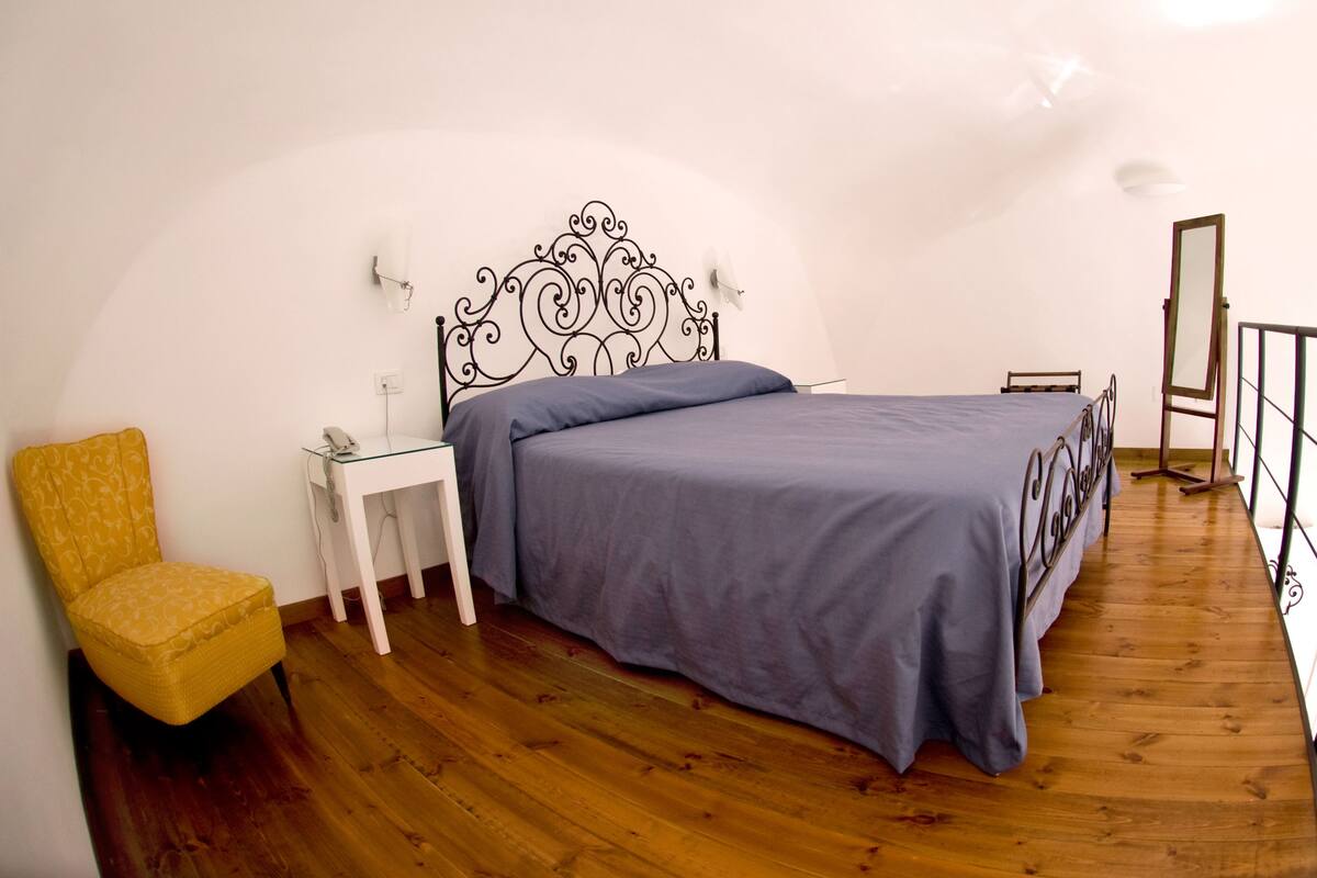 Ein Schlafzimmer mit Bett, Stuhl, Nachttisch und Spiegel.