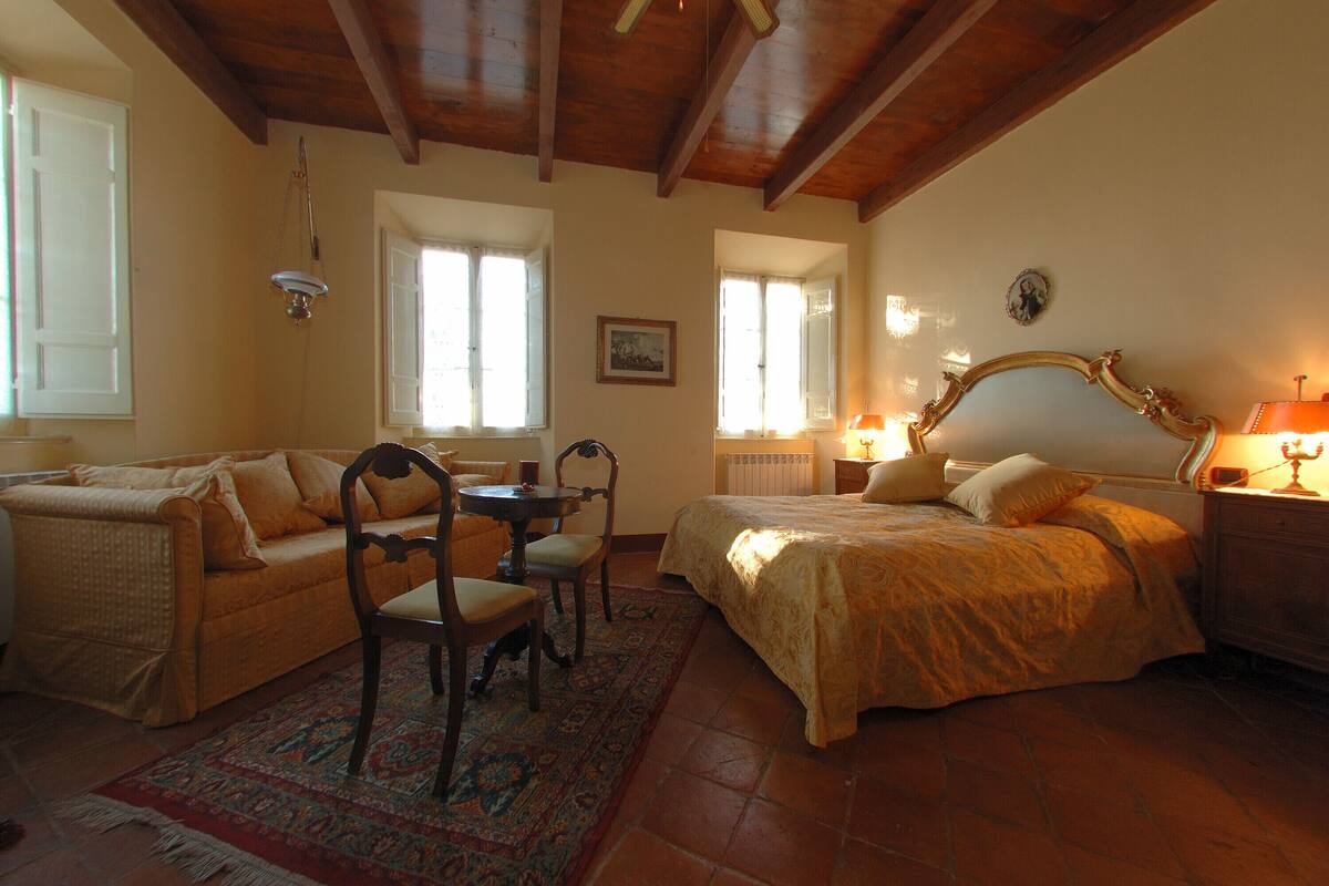 A cozy bedroom with a bed, a sofa, a small table, and chairs.