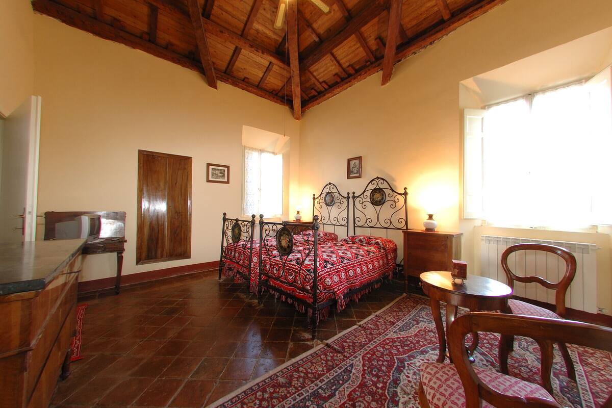 A bedroom with a four-poster bed, a wooden desk, a chair, and a radiator.