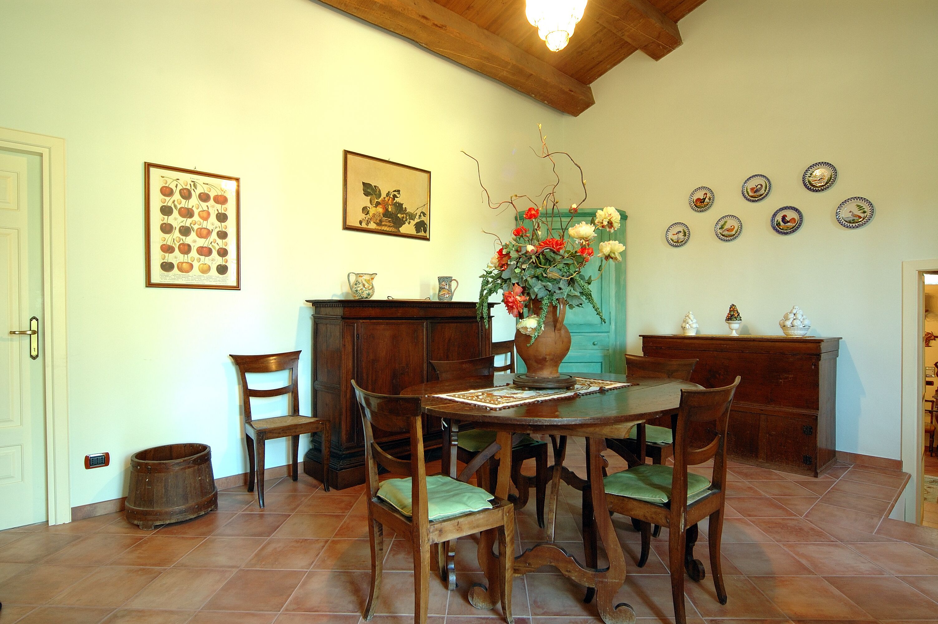 Un coin repas avec une table en bois, des chaises, un vase de fleurs et des assiettes décoratives accrochées au mur.