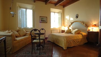 Classic room with a bed, chair, table, and sofa, featuring a large window and a wall-mounted lamp.