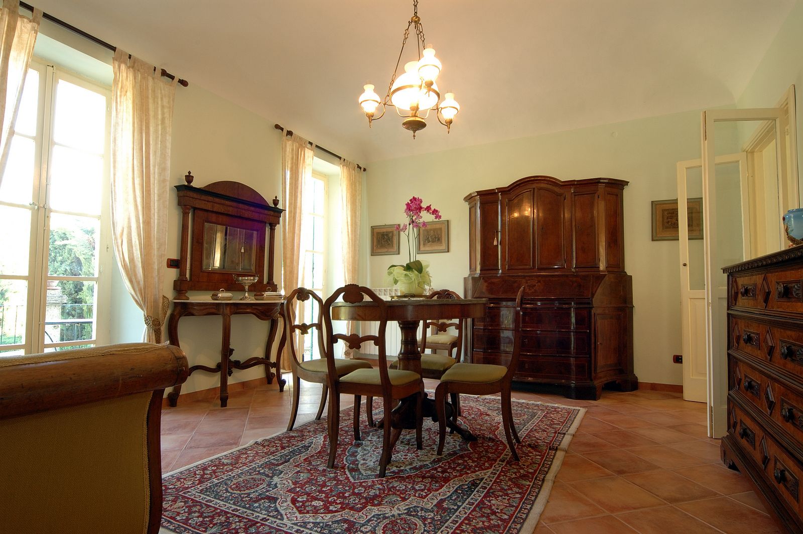 A dining room with a chandelier, wooden furniture, and a patterned rug.
