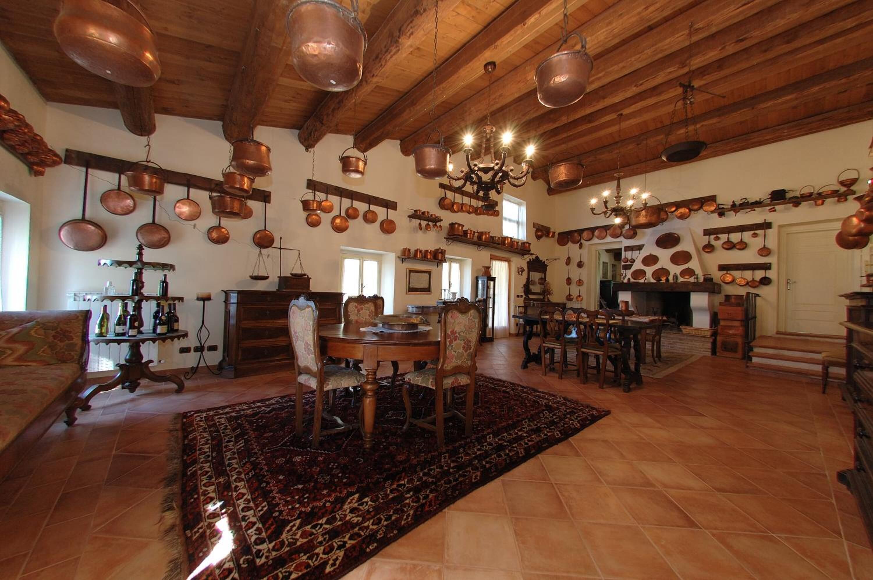 A spacious living room with a large wooden ceiling, a dining area with a round table and chairs, and a kitchen area with copper pots and pans hanging from the ceiling.