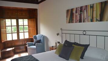 Un dormitorio con una cama, una silla, un ventanal y un cuadro en la pared.