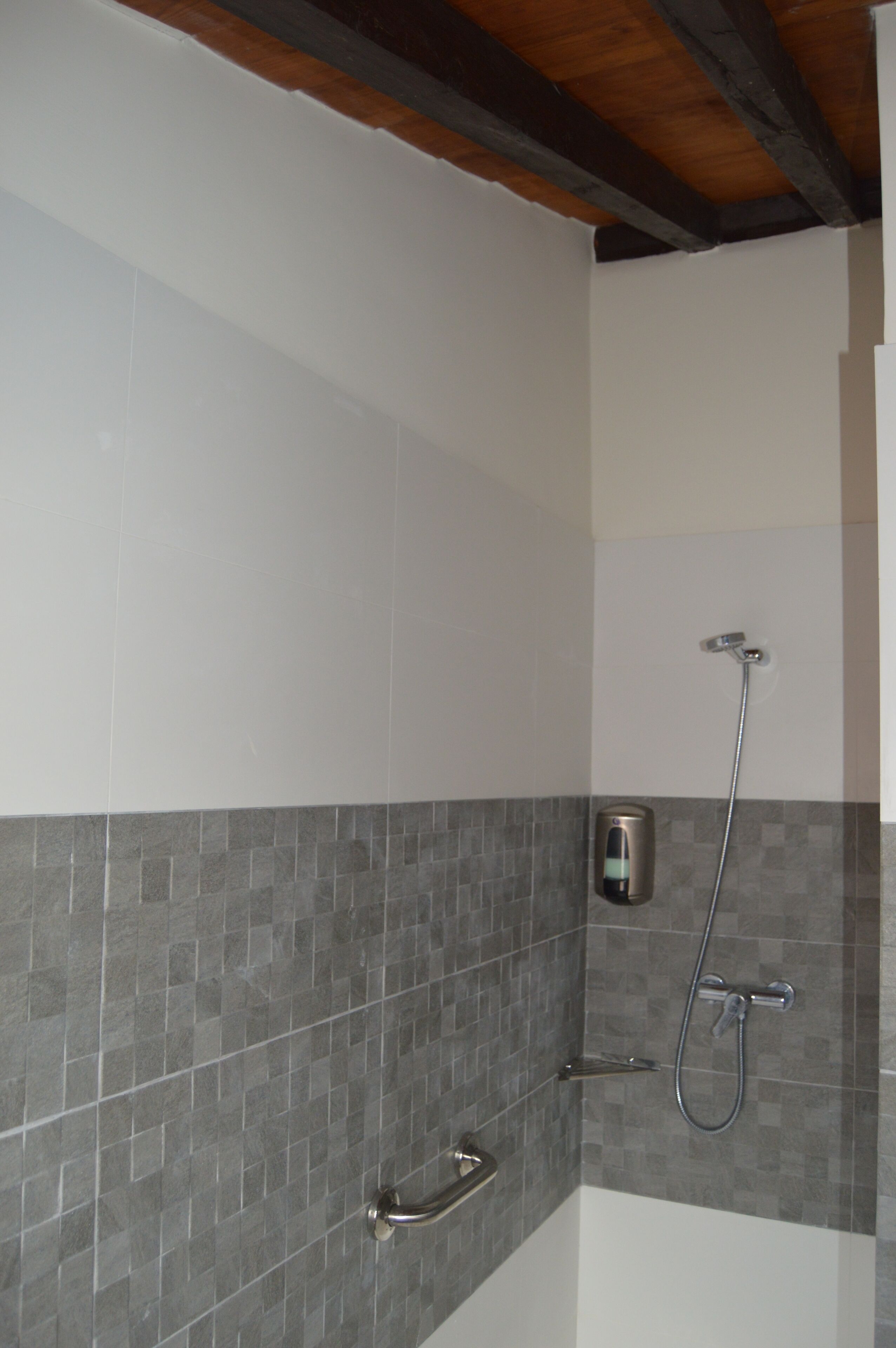 Un baño con ducha, paredes de azulejos y una viga de techo de madera.