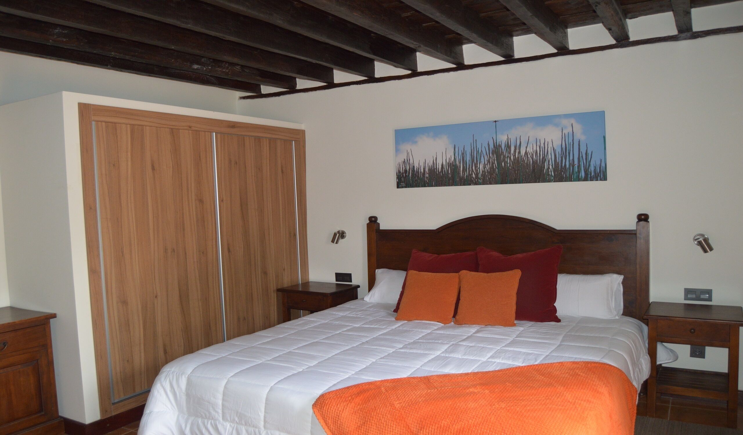 A bedroom with a wooden bed, a large wardrobe, and a painting on the wall.