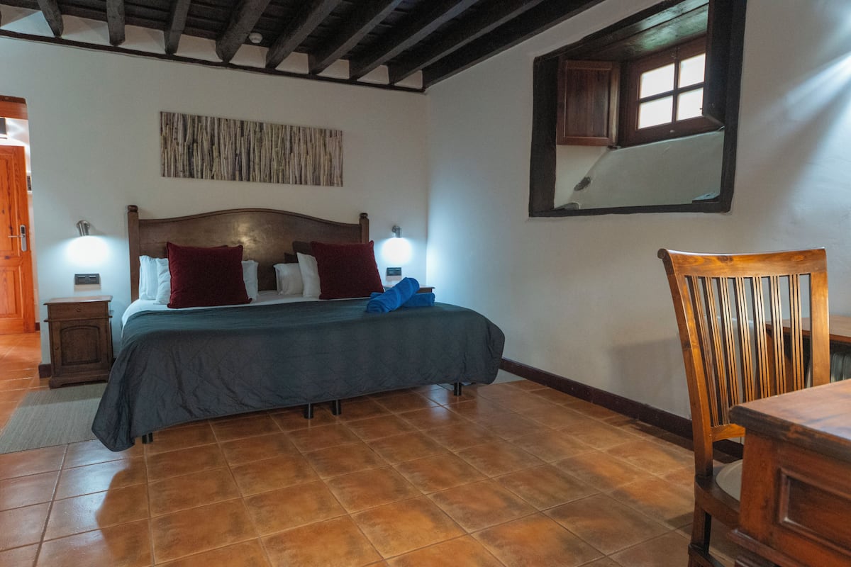 A bedroom with a wooden bed, two bedside lamps, a wooden chair, and a window with a view of the outside.