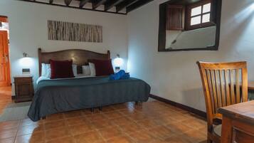 Un dormitorio con una cama de madera, dos lámparas de noche, una silla de madera y un ventanal con vistas al exterior.