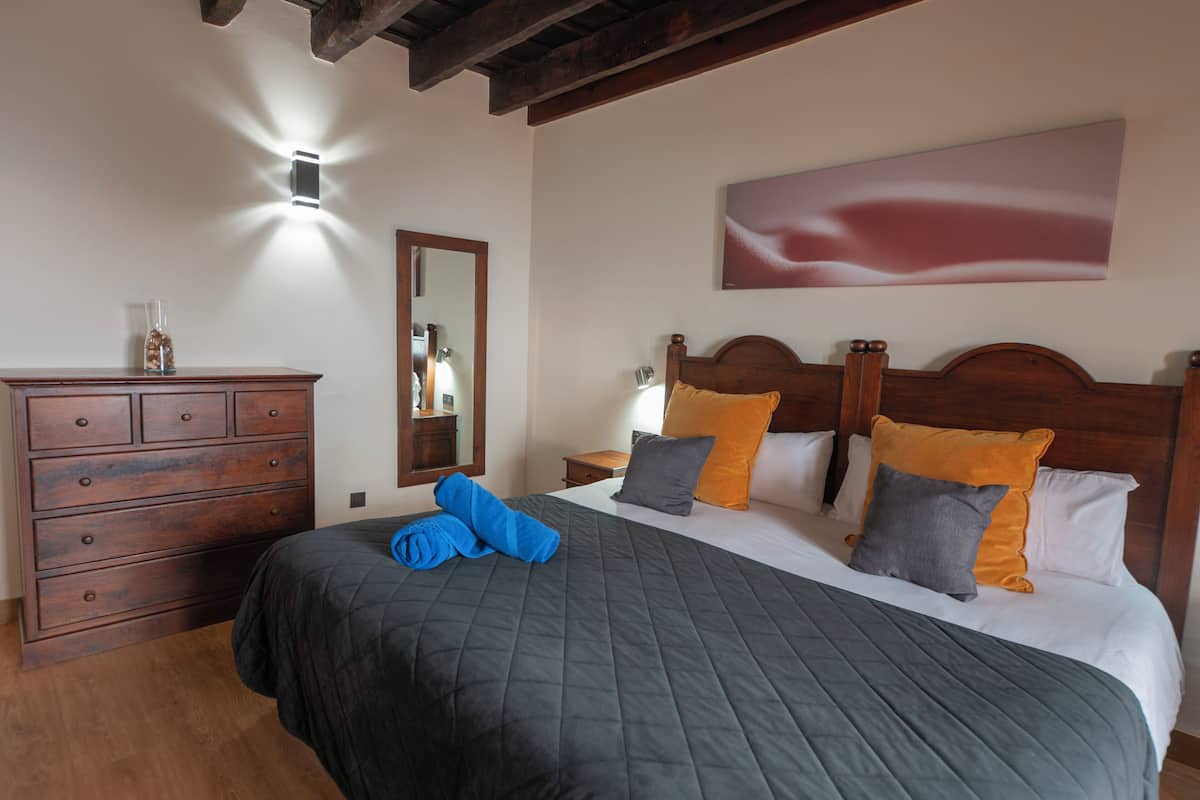 A neatly made bed with a dark quilt, wooden headboard, and multiple pillows in various colors.