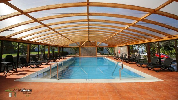 An indoor swimming pool with a wooden roof and tiled floor, surrounded by lounge chairs. - Hotel Rural Casablanca (Los Realejos)