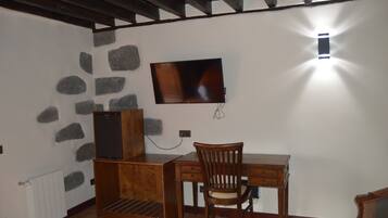 A small room with a wooden desk, a chair, a television mounted on the wall, and a stone wall feature.