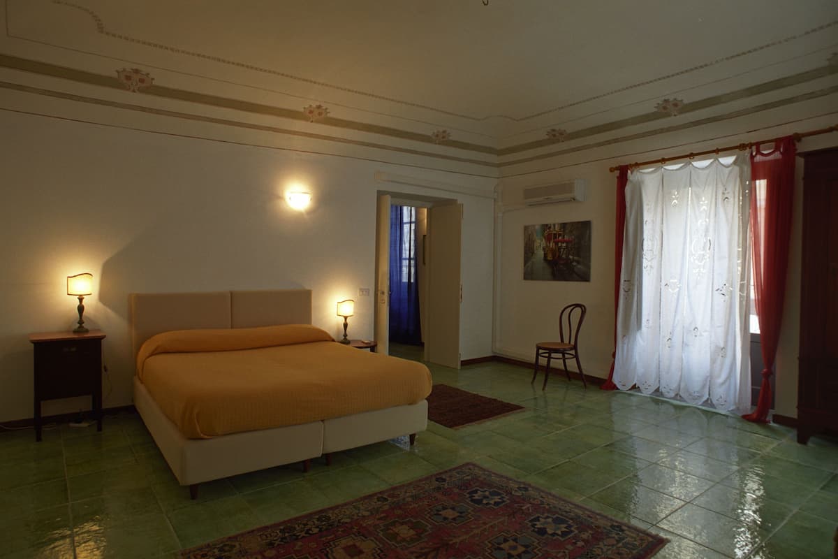 A bedroom with a bed, two bedside lamps, a chair, a door, and a window with curtains.