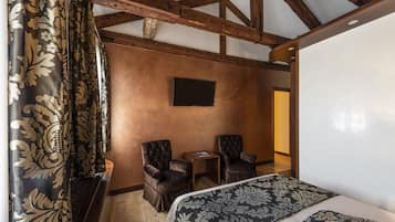 Una habitación con una cama, dos sillas, una mesita y un televisor en la pared.