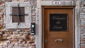 A wooden door with a sign reading "Abbazia de Luxe" and a brick wall with a window and a security device. - Abbazia De Luxe (Venice)