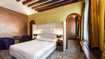 A hotel room with a large bed, two bedside tables with lamps, a small table with a vase, and a bench along the wall.
