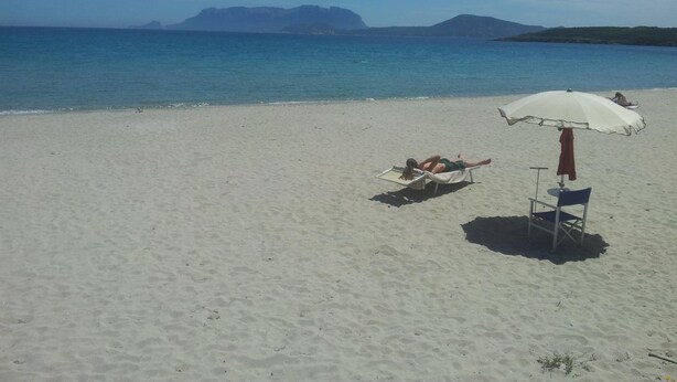 A beach with a clear view of the sea and distant mountains. There is a beach umbrella and a chair. - Hotel Demar (Olbia)