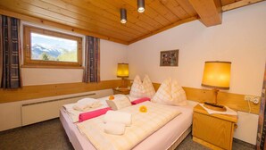 A cozy bedroom with a large bed, two bedside lamps, a window with a mountain view, and a wooden ceiling.