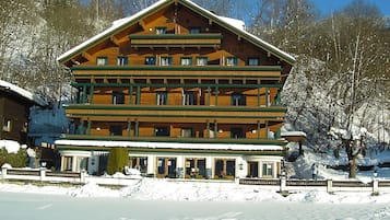 A multi-story wooden building with balconies, likely a hotel or lodge, surrounded by snow and trees.