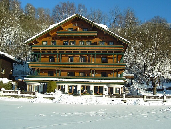 A multi-story wooden building with balconies, likely a hotel or lodge, surrounded by snow and trees. - Appartement Kitzsteinhorn (Zell am See)